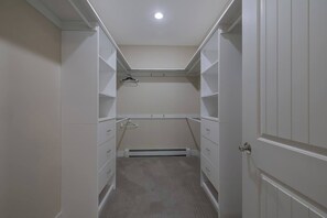 A narrow walk-through closet with white shelving, a radiator, and a door on the right.