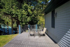 A wooden deck with a table and chairs, surrounded by trees and a house. - Spacious 5BR Home in Center of MDI [Loons Landing] (Mount Desert)