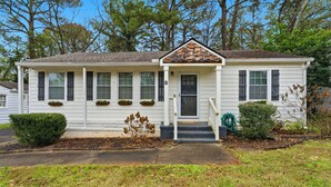 A single-story house with a front porch, a small entryway, and a front yard with a hedge and a tree. - Comfortable & Quiet 3BR Home Near Downtown ATL (Atlanta)