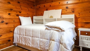 Ein Zimmer mit Holzwandverkleidung, einem Bett, einem Nachttisch und einer Regalwand.
