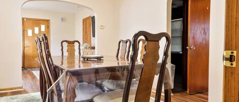 Une salle à manger avec une table rectangulaire, six chaises en bois et une nappe en verre pour la table.