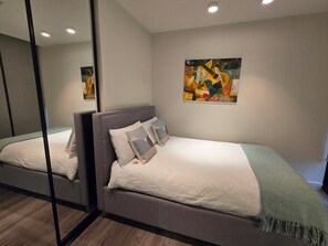 Ein modernes Schlafzimmer mit Bett, Kissen, Decke, einem Bild an der Wand und einem Spiegel.