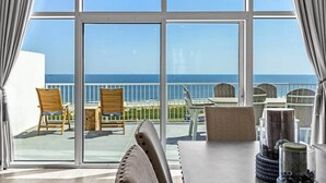Een balkon met uitzicht op de oceaan, met houten stoelen en een tafel met decoratieve objecten.