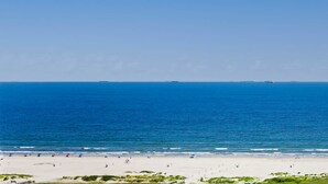 Een strand met een heldere lucht, rustige zee en een zandstrand met mensen en parasols.