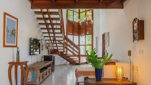 A spacious living area with a wooden staircase, a television, a wooden coffee table with a plant, and a wall-mounted clock. - Bomfim Mansion Full Amenities by Carpediem (Caucaia)