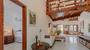 A spacious living area with a high ceiling, wooden beams, and a chandelier. There is a sofa set, a coffee table, and a dining area with a wooden table and chairs. - Bomfim Mansion Full Amenities by Carpediem (Caucaia)