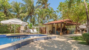 A swimming pool with tiled edges, surrounded by palm trees and a covered patio area with outdoor seating. - Bomfim Mansion Full Amenities by Carpediem (Caucaia)