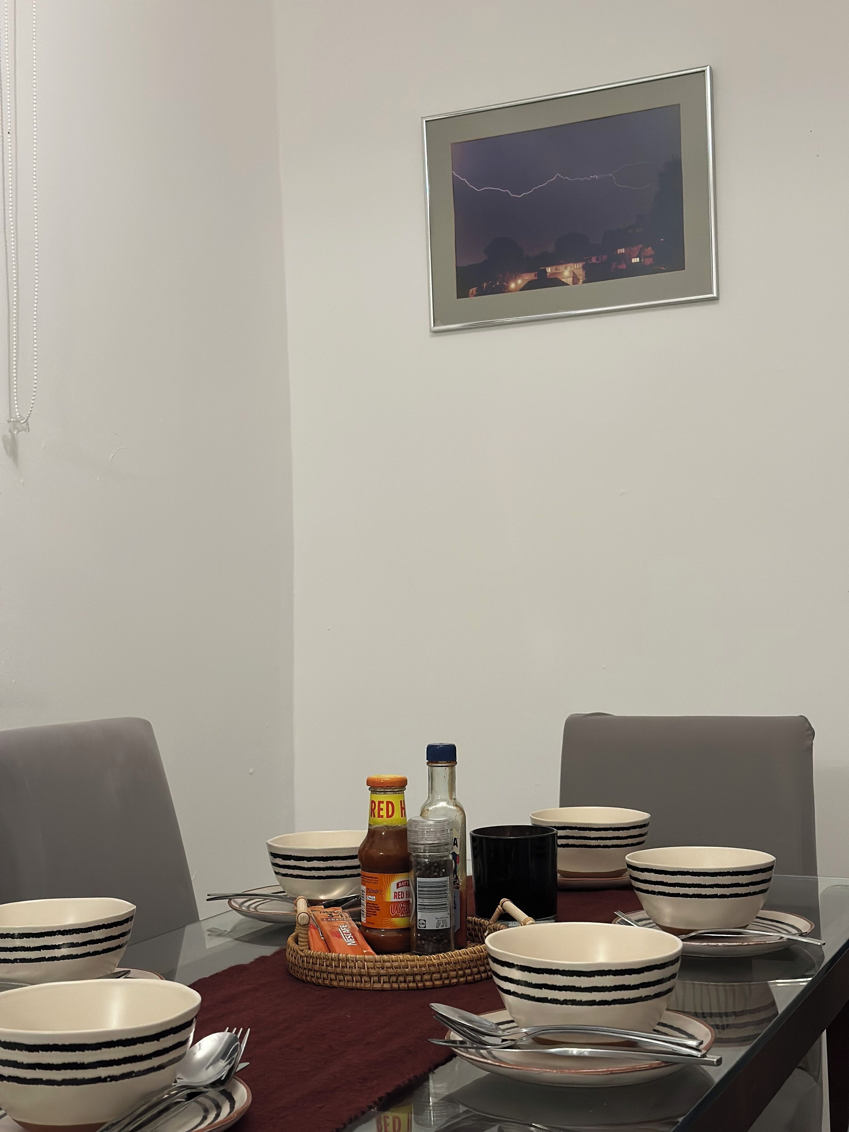 A dining table set with striped bowls, plates, and cutlery, with condiments and a bottle on a tray.