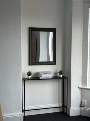 A corner of a room with a black console table, two potted plants, and a framed mirror above it. - The Manger
Stylish 3-Bed Coastal Home with Scandinavian Charm (Gorleston-on-Sea)