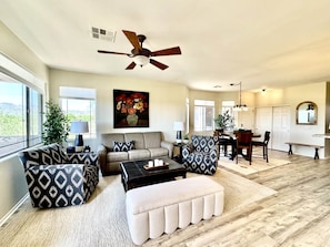 A spacious living room with a ceiling fan, a dining area with a table and chairs, and a large window offering a view of the outdoors. - Vistoso Condo #212C (Oro Valley)