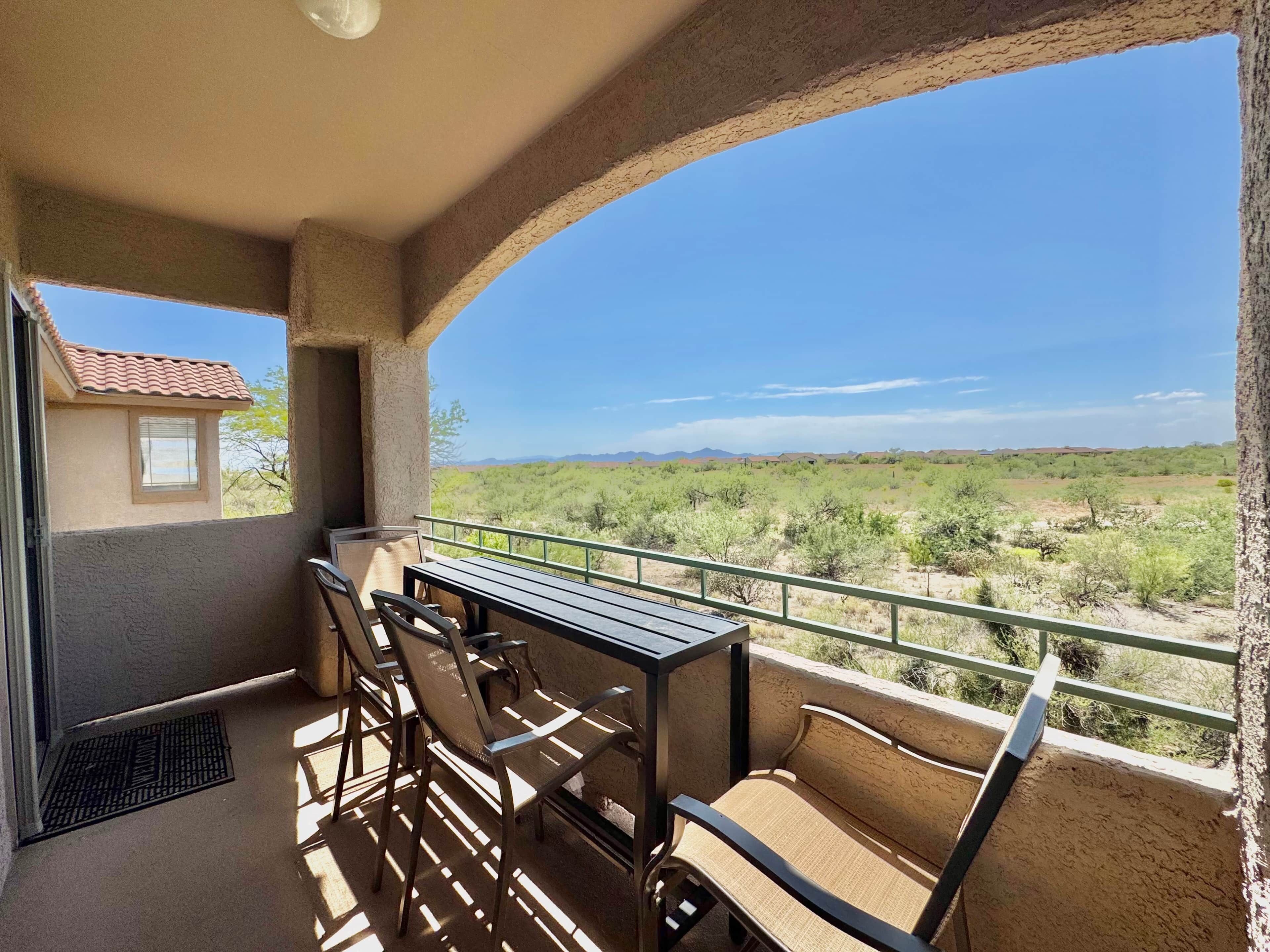 A balcony with a table and chairs, overlooking a desert landscape.