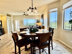 A dining area with a round table, chairs, a chandelier, and large windows with a view. - Vistoso Condo #212C (Oro Valley)