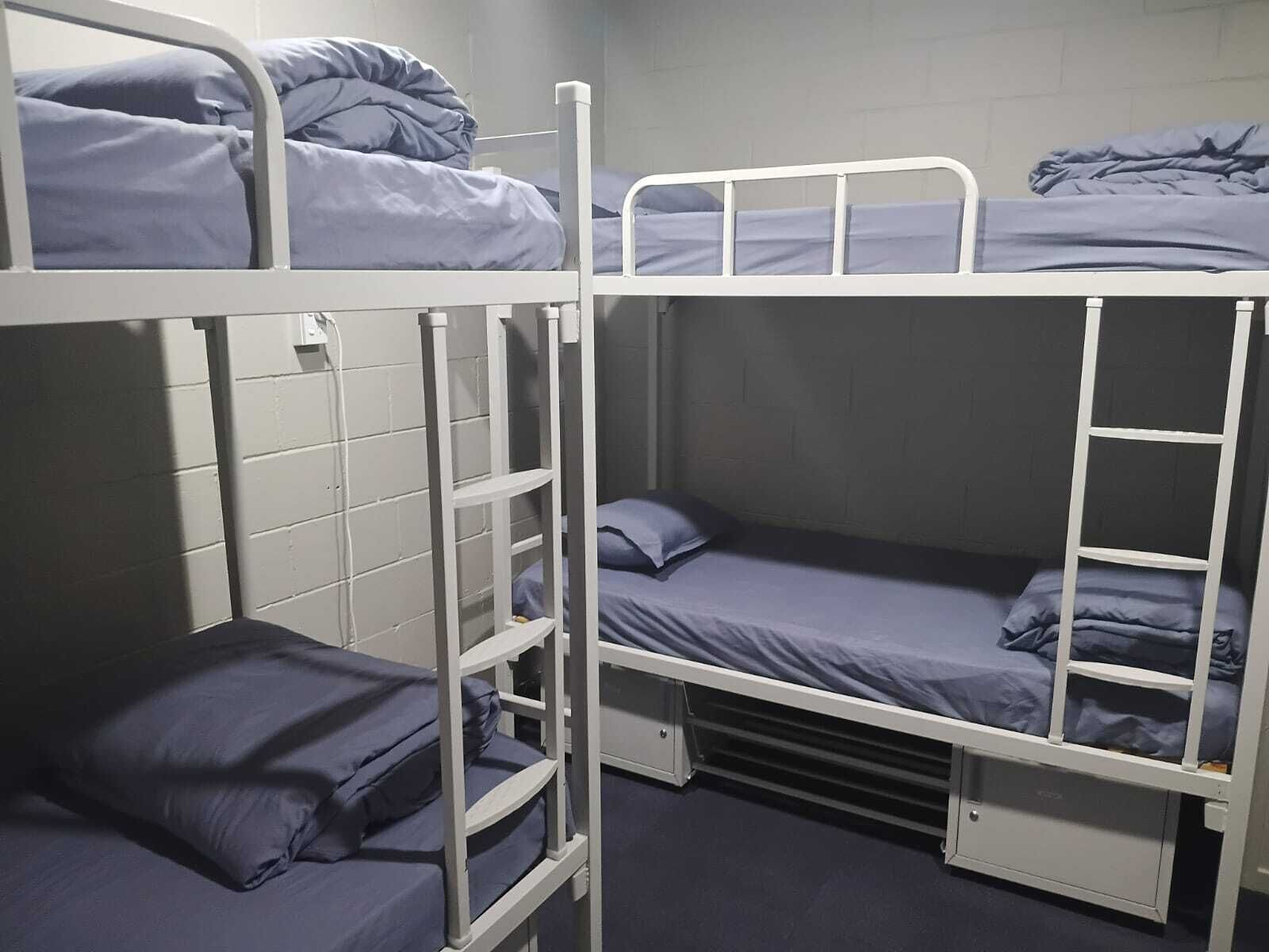Een slaapkamer met een stapelbed, een klein opbergkastje en een wandplank.