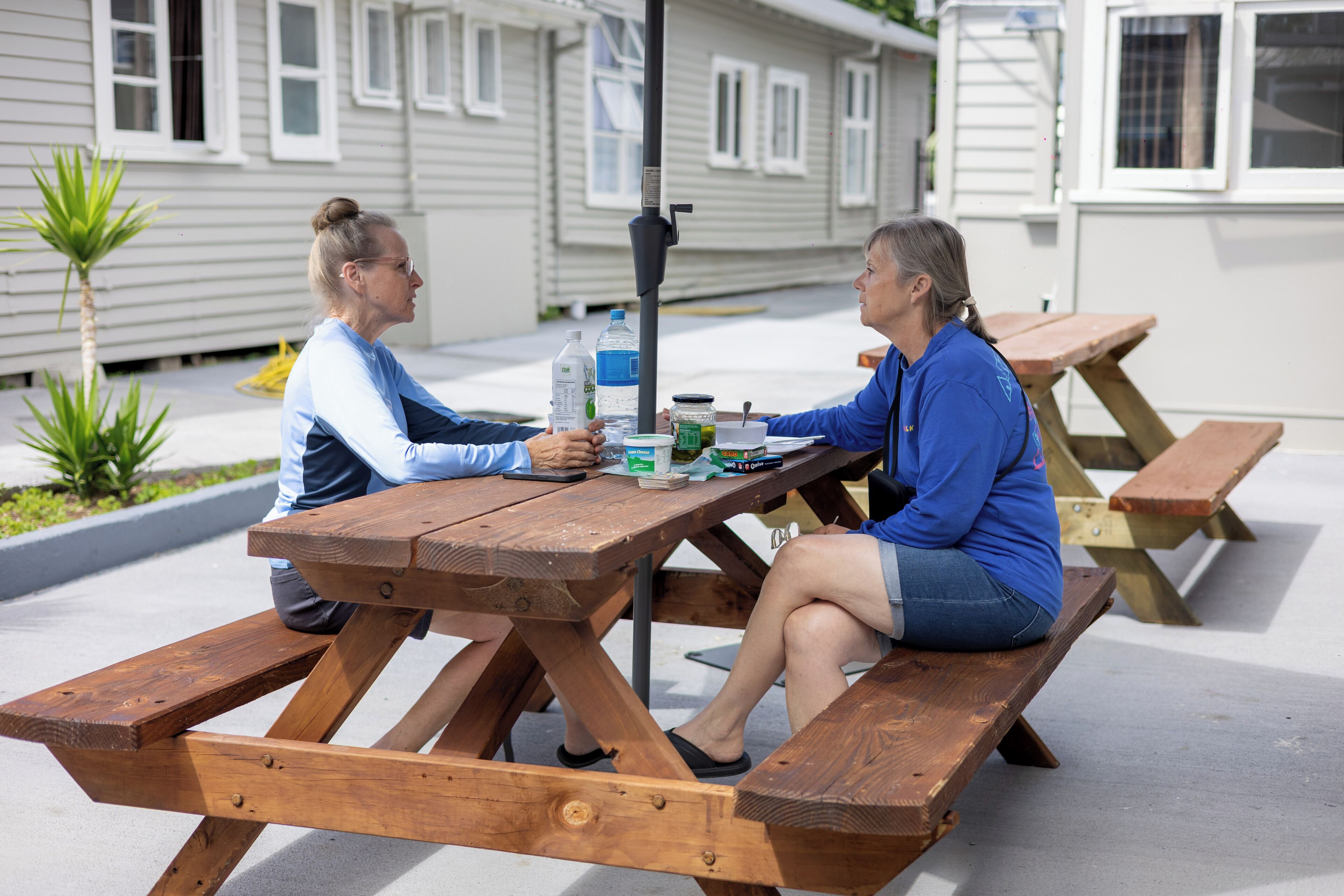 Two people seated at a wooden picnic table with a water bottle, a book, and a smartphone on it.