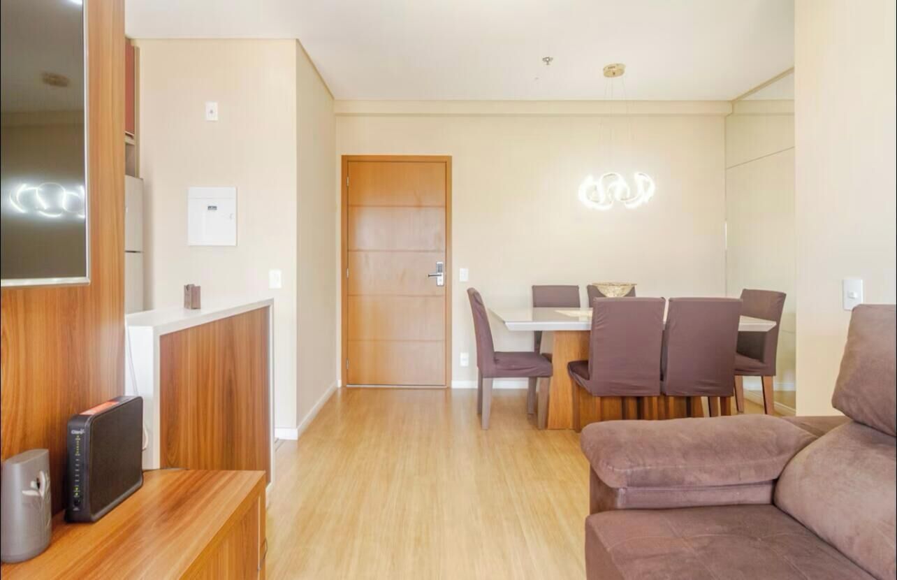 Una sala de estar moderna con un mostrador de recepción de madera, una zona de comedor con una mesa y sillas, y un televisor de pantalla plana grande montado en la pared.