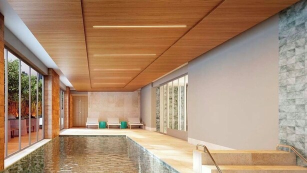 Une piscine intérieure spacieuse offrant une vue dégagée sur l’extérieur, un mur en pierre et un escalier menant à un niveau supérieur.