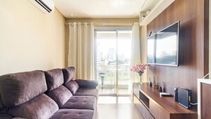 Un salon moderne avec un canapé, un téléviseur à écran plat et une porte-fenêtre coulissante donnant sur un balcon.
