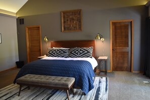 Een slaapkamer met een bed, een bankje, nachtkastjes, lampen en een deur.