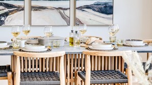 Une table à manger dressée avec des assiettes, des verres et des verres à vin, entourée de chaises en bois dont les assises sont en osier tressé.