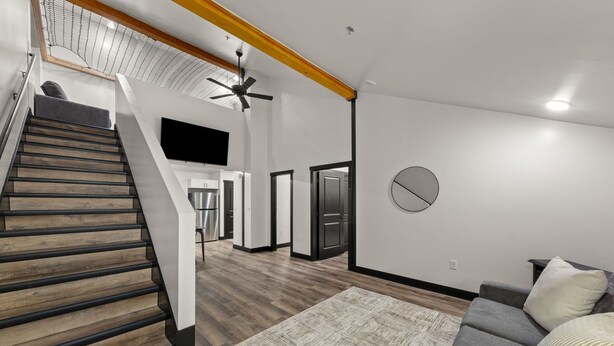 Um interior moderno com uma escada, uma sala de estar com sofá e uma cozinha ao fundo.