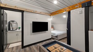 Quarto moderno com televisão de tela plana, uma cama, pequeno espaço de cozinha e teto de madeira.