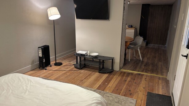 A hotel room with a bed, a desk with a lamp, a TV, and a wooden floor. - Cozy Private Studio w/ Kitchenette (Pittsburgh)