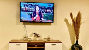 Televisão fixada na parede acima de um console de madeira com gavetas e objetos decorativos.