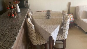 Uma área de refeições com uma mesa coberta por um toalha de renda, rodeada por cadeiras estampadas.