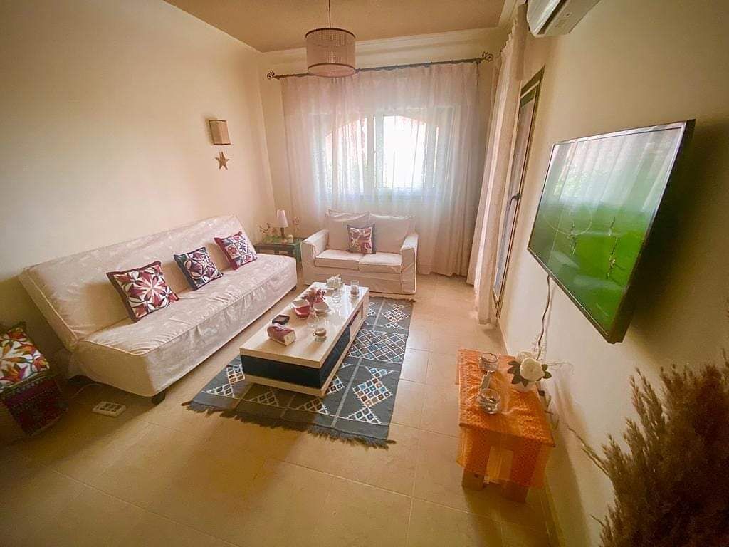Uma sala de estar com sofá, mesa de centro, televisão e janela com cortinas.