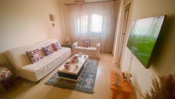 Uma sala de estar com sofá, mesa de centro, televisão e janela com cortinas.