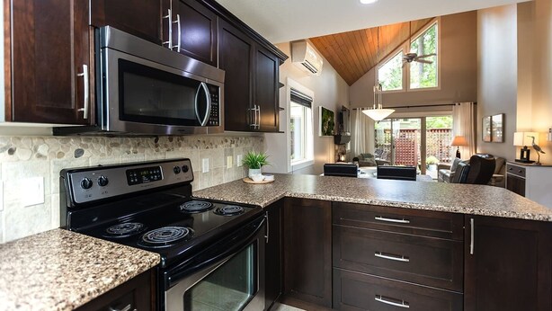 A modern kitchen with dark wood cabinets, a granite countertop, a stainless steel stove, and a microwave. - Cottage at Oceanside Village Resort - Sandpiper (Parksville)