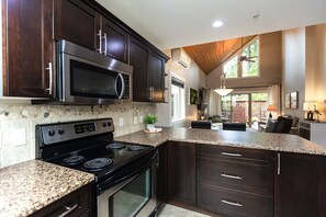 A modern kitchen with dark wood cabinets, a granite countertop, a stainless steel stove, and a microwave. - Cottage at Oceanside Village Resort - Sandpiper (Parksville)