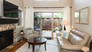 A living room with a fireplace, a sofa, a coffee table, and a TV mounted on the wall. - Cottage at Oceanside Village Resort - Sandpiper (Parksville)