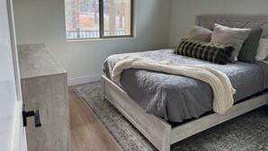 Ein Schlafzimmer mit einem Bett, einem Fenster und Blick auf Bäume.