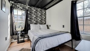 Un dormitori amb un llit, una tauleta de nit, una finestra amb cortines i un paper pintat amb motius.