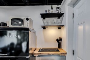 Ett kompakt kök med en Galanz-mikrovågsugn, en inbyggd spis och en hylla med glas och flaskor.
