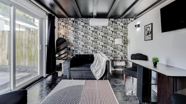 Un saló modern amb un sofà negre, una zona de menjador amb taula i cadires, un paper pintat i un finestral gran.