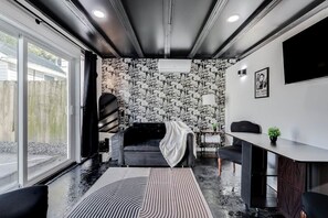 Ett modernt vardagsrum med en svart soffa, en matplats med bord och stolar, en mönstrad tapet och ett stort fönster.