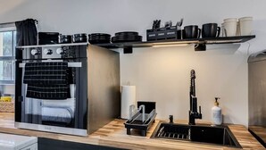 Una cuina moderna amb forn integrat, un rentatalls i una estant amb utensilis de cuina i plats.
