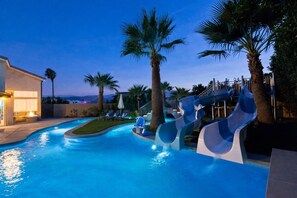 Una piscina con scivoli, palme e lettini.