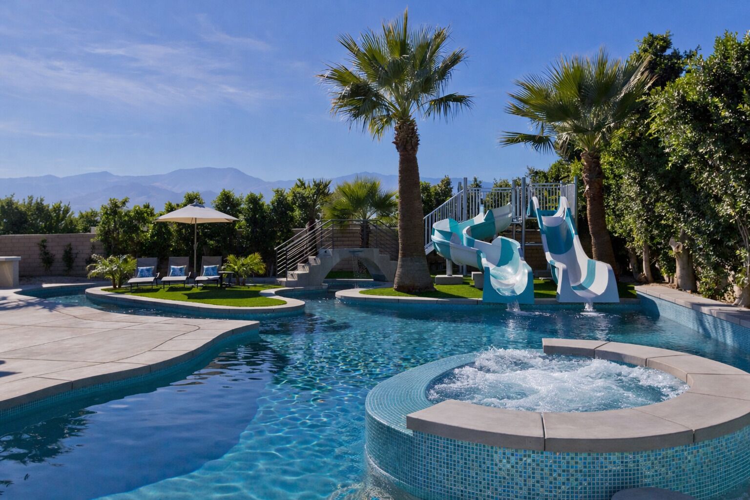 Une piscine avec un jacuzzi, des toboggans, des palmiers et une vue sur les montagnes.