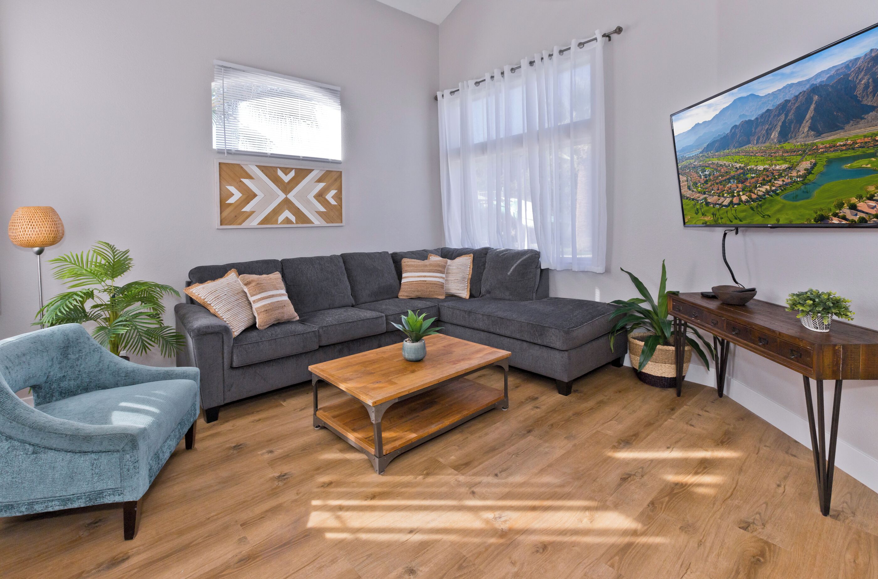 A modern living room with a grey sofa, a wooden coffee table, a blue armchair, and a TV mounted on the wall.