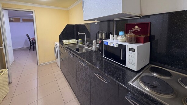 Une cuisine compacte équipée d’un four à micro-ondes, d’un évier et d’une cuisinière. Une petite fenêtre et une porte donnent accès à une autre pièce.