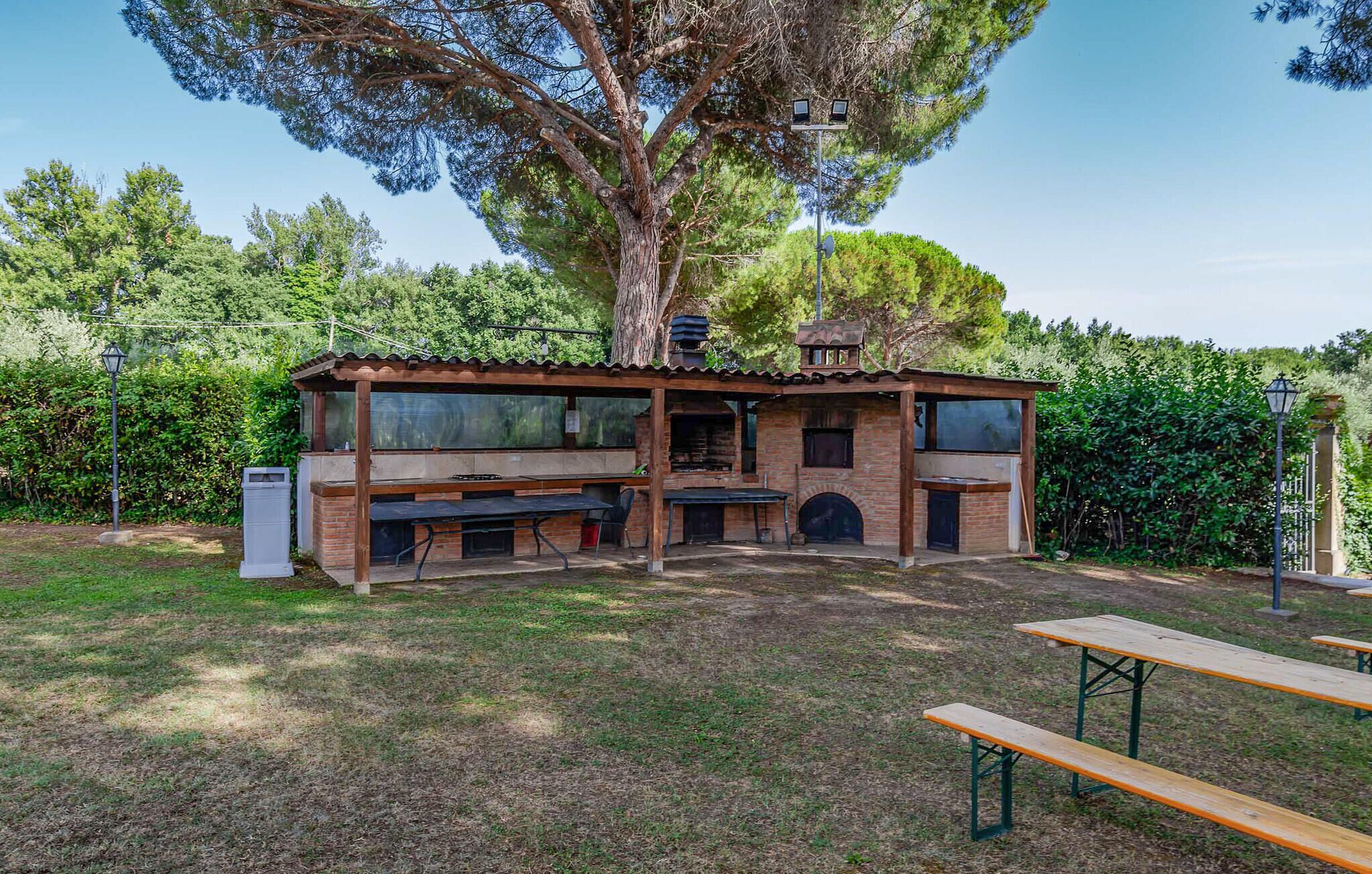 A rustic outdoor kitchen with a brick structure, a large tree, and a picnic table.
