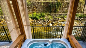 A hot tub with a stone wall and greenery in the background. - Pool•Riverfront Cabin•Walk to Gatlinburg Strip (Gatlinburg)