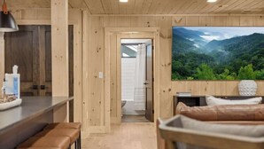 A wooden interior with a kitchen area, a bar, and a large window with a mountain view. - Pool•Riverfront Cabin•Walk to Gatlinburg Strip (Gatlinburg)