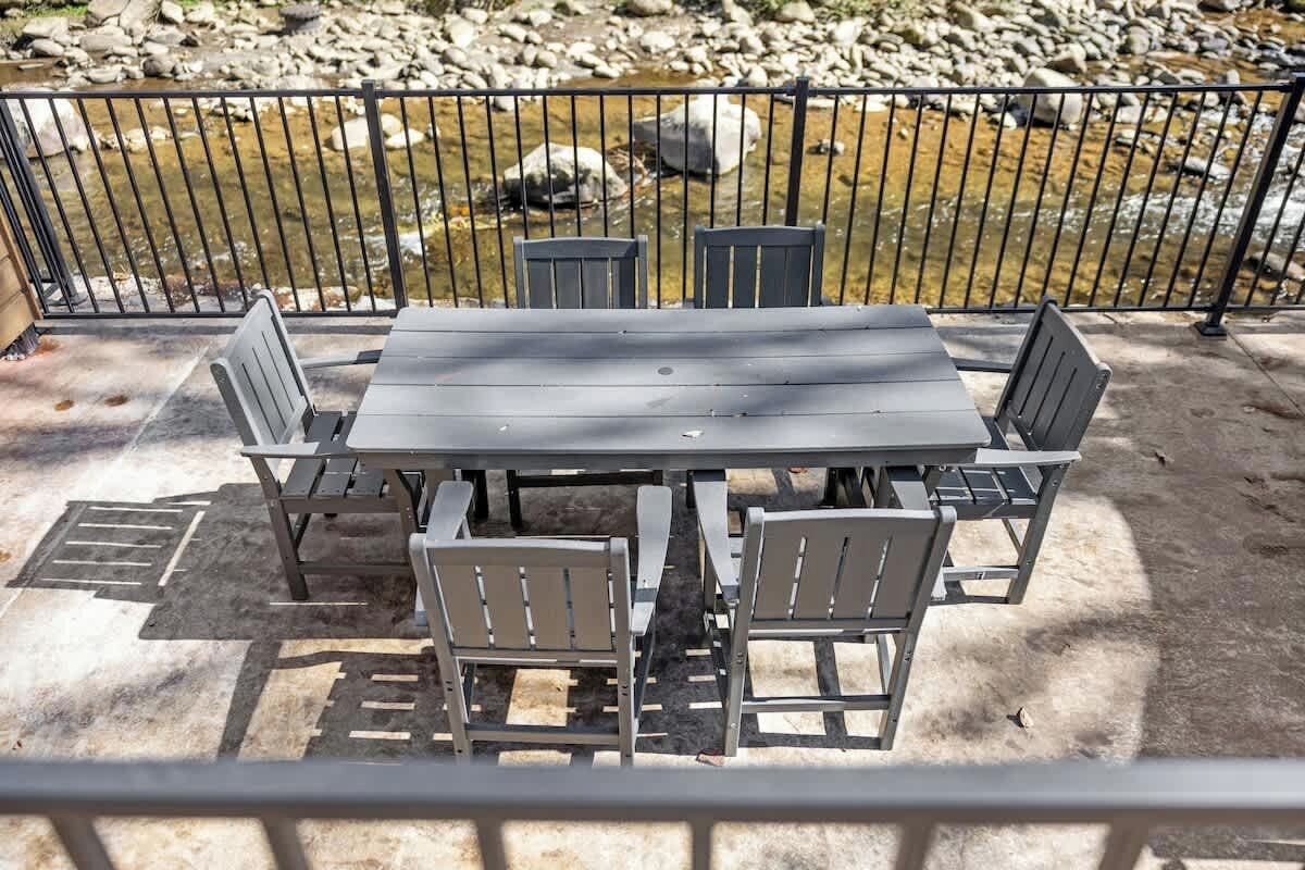 An outdoor patio with a table and chairs, a metal fence, and a rocky stream in the background.