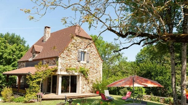 Una casa de piedra con porche cubierto, mobiliario exterior y jardín.