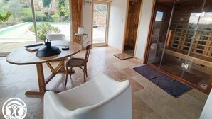 Una habitación moderna con techo de madera, una mesa redonda con una silla, una puerta de vidrio que da al exterior y vista a una piscina.