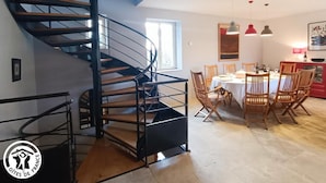 Un interior moderno con una escalera de caracol, una zona de comedor con sillas de madera y una cocina.